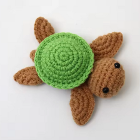 Crocheted turtle toy with a green shell on a white background